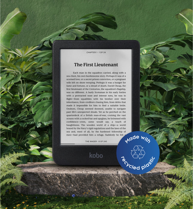 A Kobo Clara BW eReader with a label that reads "Made with recycled plastic", set on a stone in foliage.